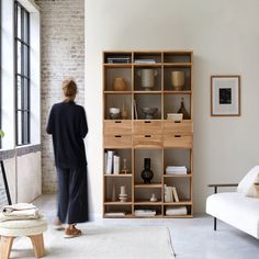 a person standing in front of a book shelf with books and vases on it