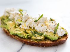 an avocado toast topped with feta cheese and chives on a marble surface