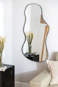 a mirror sitting on top of a wall next to a chair and vase filled with flowers