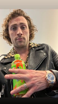 a man in a leather jacket is holding a bottle and pointing at the camera with his finger