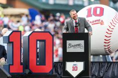 a man standing at a podium in front of a large baseball sign with the number 10 on it