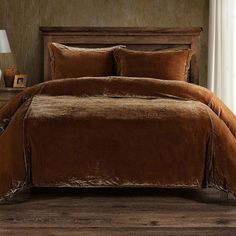 a bed with brown comforter and pillows in a room next to a lamp on a table