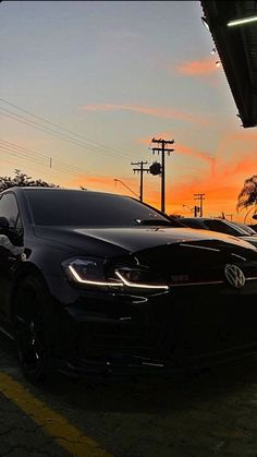 a black car parked in front of a building with the sun going down behind it