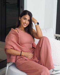 a woman sitting on top of a white couch wearing a pink dress and matching watch