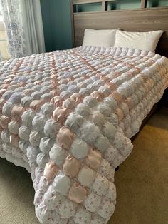 a large bed covered in pink and white ruffles next to a window with curtains