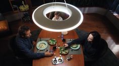 two people sitting at a table with plates of food in front of them and a large light hanging above them