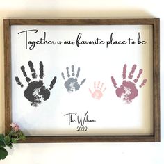 two handprints are displayed in a frame on the wall next to a plant