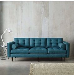 a blue couch sitting next to a lamp on top of a wooden table in front of a white wall