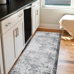 a kitchen area with white cabinets and black counter tops, along with a rug on the floor