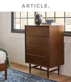 a wooden dresser sitting in front of a window next to a blue rug and chair