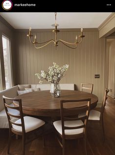 a dining room table and chairs with flowers in a vase on the center, next to a couch