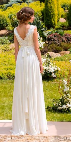 a woman in a wedding dress looking out over the garden at flowers and greenery