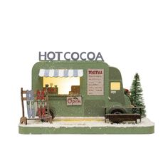 a small green food truck parked in front of a building with a sign that says hot cocoa