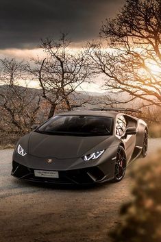 a dark colored sports car parked on the side of a road with trees in the background