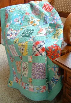 a bed with a quilt on top of it next to a chair and wooden headboard