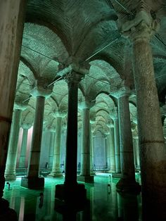 the inside of an old building with columns and lights shining on the floor, along with green water