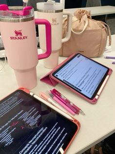 the tablet is next to a pink cup and coffee mug on the table with it's lid open