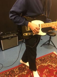 a person playing an electric guitar in a room with blue carpet and red rugs