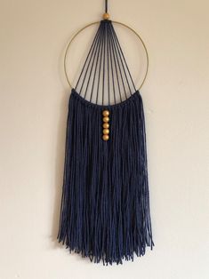 a blue wall hanging with wooden beads and fringes on the end, in front of a white wall