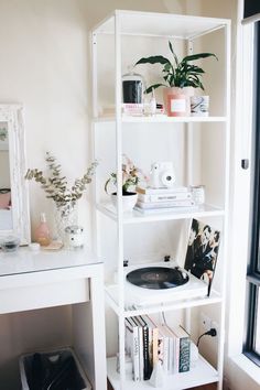 a white shelf filled with books and plants next to a mirror on top of a wooden floor