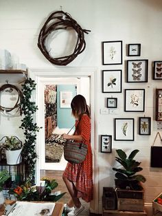 a woman in a red dress is holding a wicker basket and looking at pictures on the wall