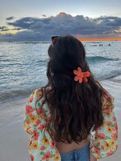 a woman standing on top of a beach next to the ocean with a flower in her hair