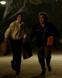 two young men walking down the street at night carrying shopping bags and paper bags in their hands