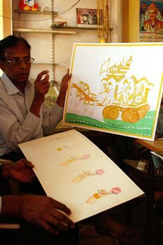 a man sitting in front of a white board holding up a drawing on it's side