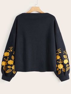 a black sweatshirt with gold embroidered flowers on the sleeves and cuffs, hanging from a hanger