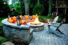 an outdoor fire pit surrounded by chairs and tables with orange pillows on it's sides