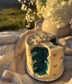 a blue and white cake sitting on top of a blanket next to a vase with flowers