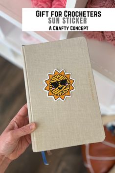 a hand holding a notebook with the words gift for crocheters sun sticker on it