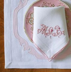 an embroidered monogrammed napkin on a pink and white plate