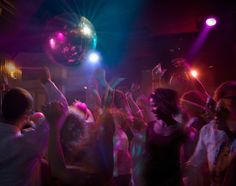 a group of people dancing at a party with disco balls in the air and lights on