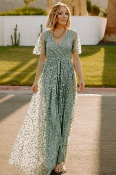 a woman in a long dress is walking down the street with her hand on her hip