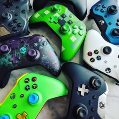 several different colored video game controllers sitting on a table with black, white and green buttons