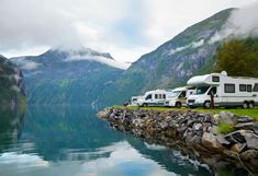 two rvs parked next to each other on the shore of a lake with mountains in the background