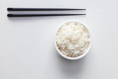 two black chopsticks are next to a small bowl of rice