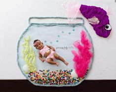 a baby in a pink swimsuit laying on top of a fish bowl filled with candy