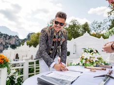 a man signing a document on top of a table with flowers and greenery in the background