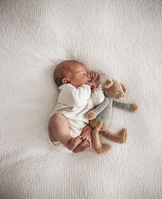 a baby laying on top of a white blanket next to a teddy bear and a stuffed animal