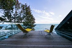 two yellow chairs sitting on top of a wooden deck next to the ocean and trees