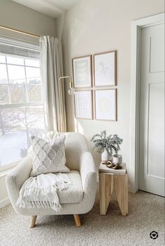 a white chair sitting in front of a window next to a table with flowers on it