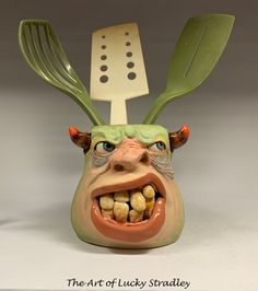 a ceramic head with two forks sticking out of it's mouth and an odd face