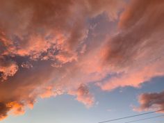 the sky is filled with pink clouds as the sun sets over power lines and telephone poles