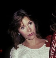 two women standing next to each other in front of a dark background with one woman wearing a red and white sweater