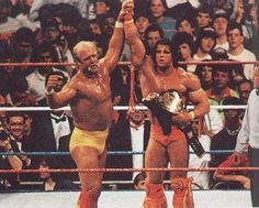 two men in wrestling gear holding up their hands and standing next to each other with people watching