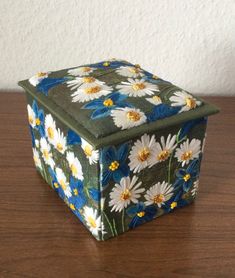 a painted box sitting on top of a wooden table next to a white and yellow flower