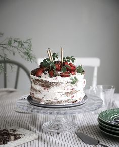 a cake sitting on top of a glass plate covered in frosting and strawberries