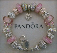 a pink and white bracelet with charms on it's side is displayed in a box